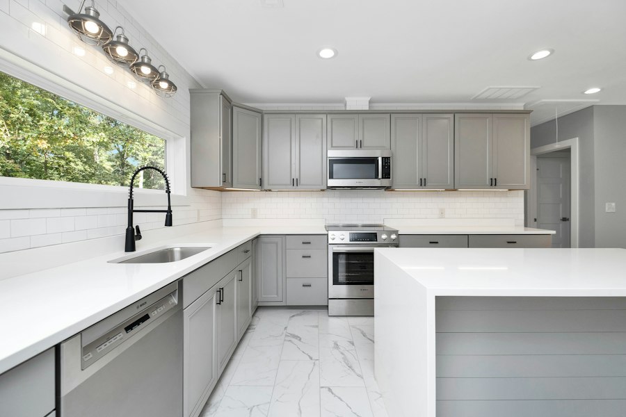 Kitchen with grey shaker cabinets, white counters and a window over the sink